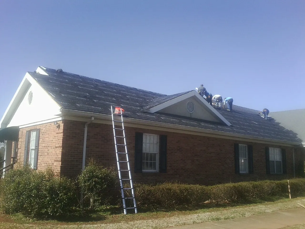 Crew tearing shingles off a brick ranch roof with a ladder set — Metal Roof Repair work by our crew in Derby