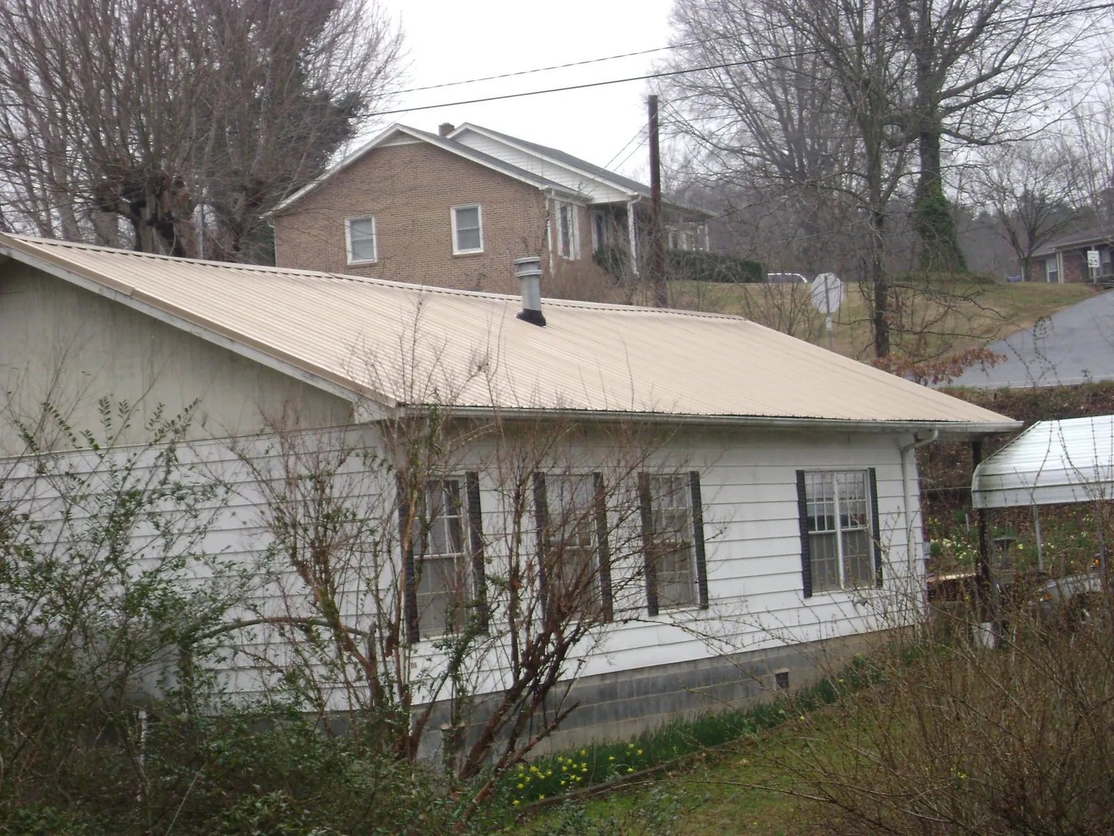 Tan metal roof on a white sided house set into a hillside — Commercial Roofing by Roofing Brothers in Derby